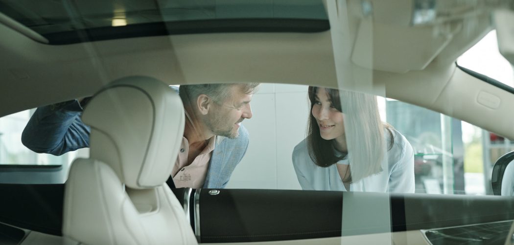 Happy customers standing by new car in auto center and bending forwards to window while looking at one another and expressing contentment